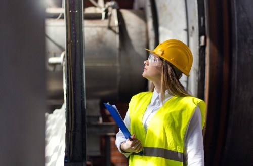 Woman with hard hat and clipboard looking off to side in industrial location