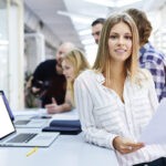 Woman in an office environment looking t camera with coworkers behind her