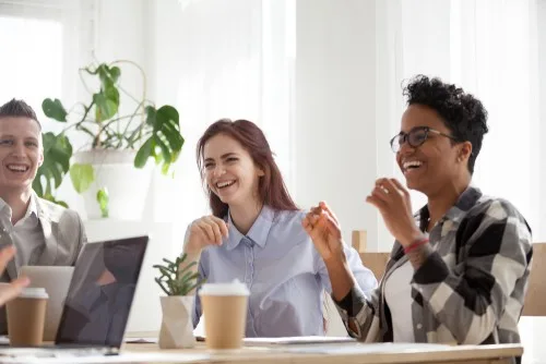 Three employees, two female and one male, laugh together in the workplace