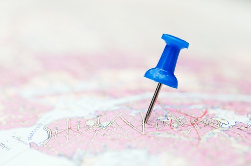 Thumbtack pinpointing a city on a map; city is indistinct.