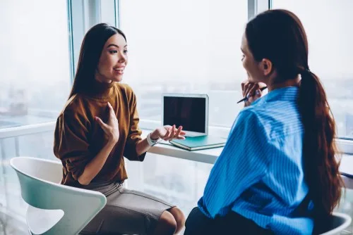 Two women having a conversation seated in a business setting