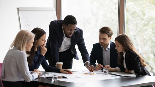 Group of individuals in office gathered around a table looking at papers