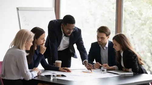 Group of individuals in office gathered around a table looking at papers